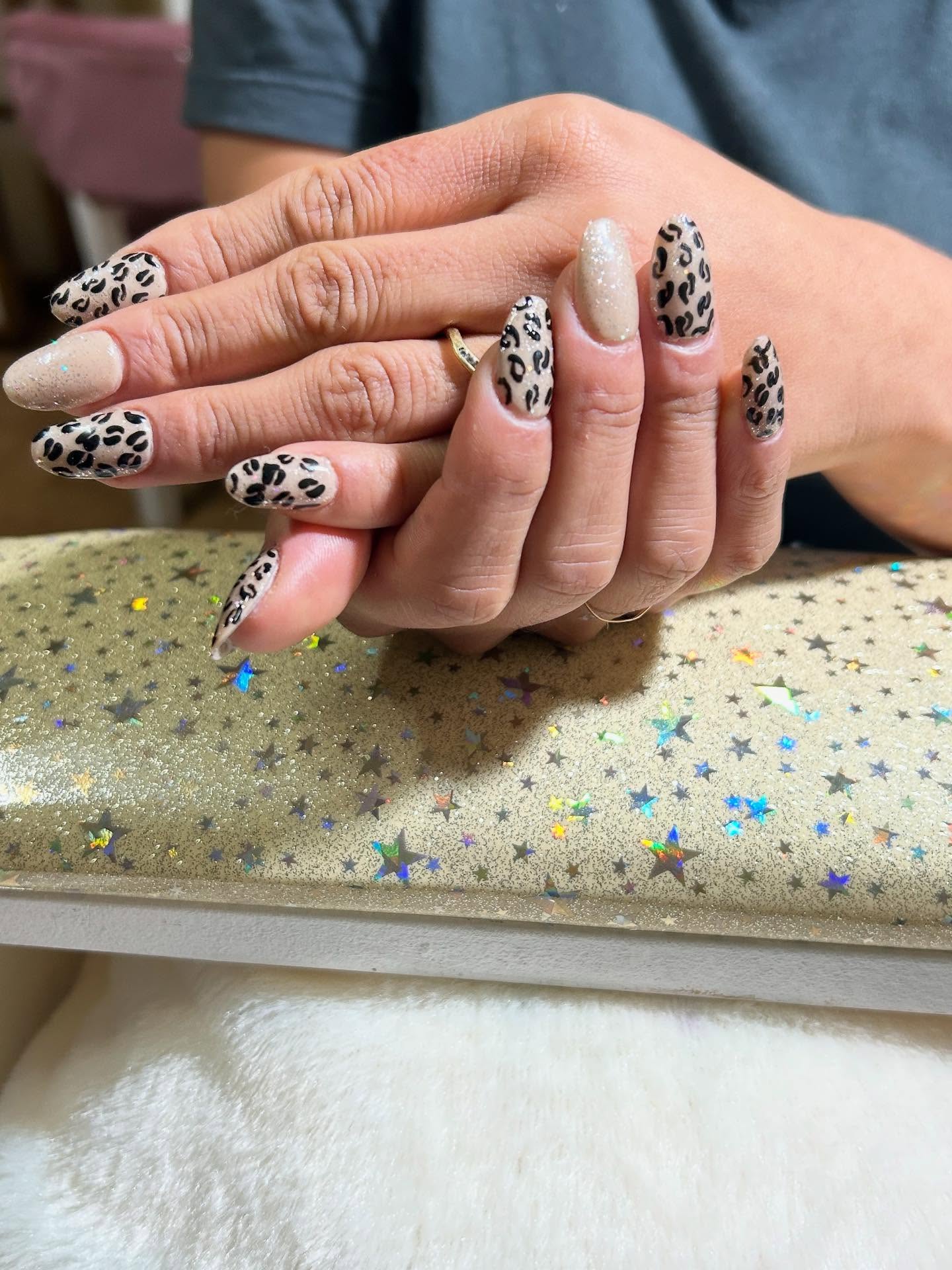 Uñas almendradas con animal print sobre base nude con glitter, apoyadas en un apoyamanos dorado con estrellas