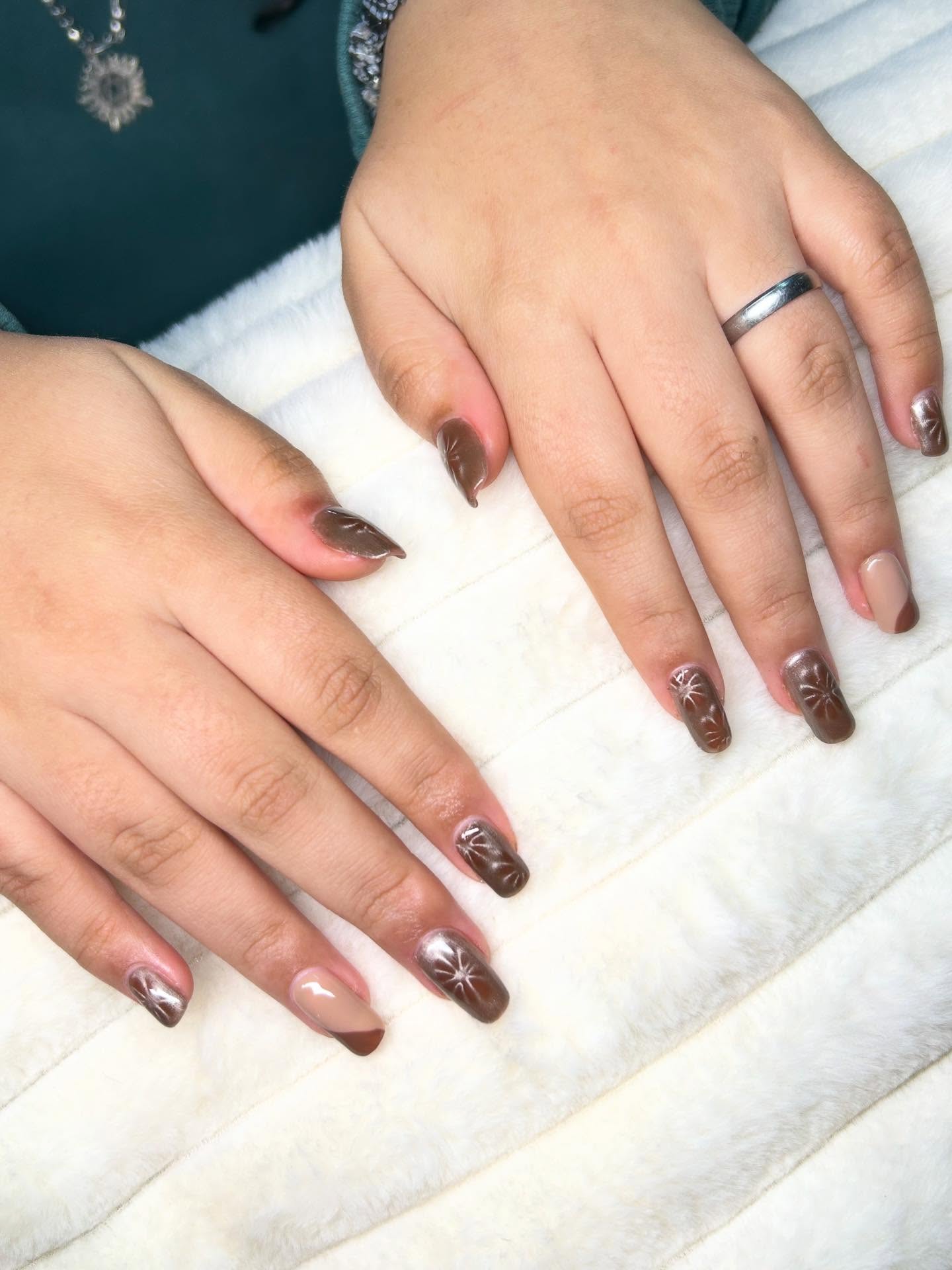 Uñas color chocolate con efecto cromado y destellos pintados, y dos uñas nude con borde chocolate, sobre una manta de piel blanca