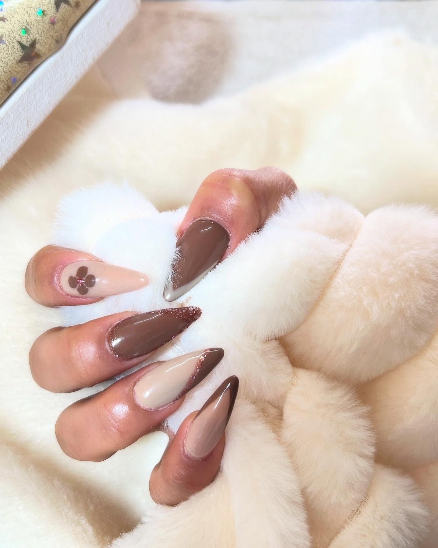 Uñas stiletto en nude y chocolate con una flor pintada, trabajo de SG Estética Integral, sobre una manta de piel blanca
